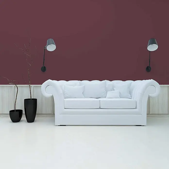 Tadessi Wandfarbe Backstein - Rot, Matt, 2,5 l - Weißes Polstersofa mit Kissen in einem stilvollen Raum mit bordeauxroter Wand und hellem Boden.