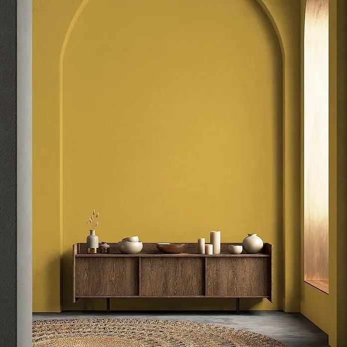 Tadessi Wandfarbe Leinen - Gelb, Matt, 2,5 l - Dunkles Holz-Sideboard mit Deko-Artikeln vor gelber Bogenwand.