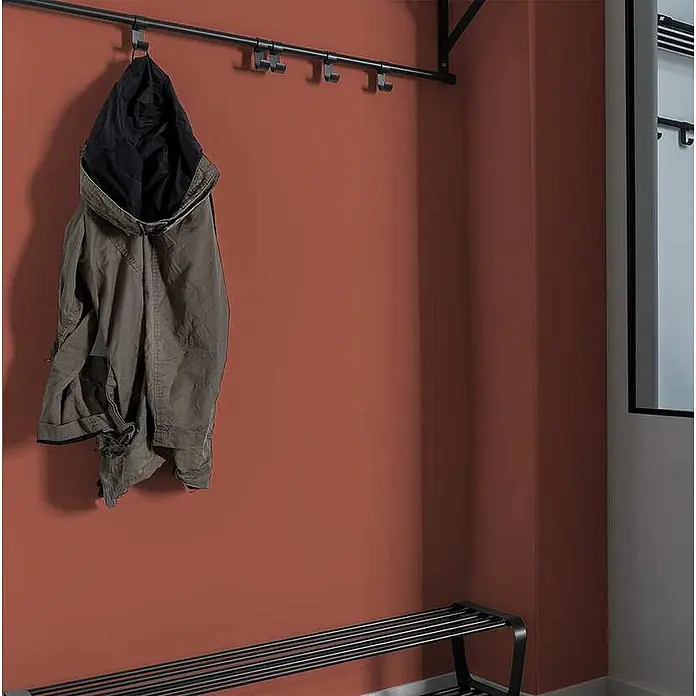 Tadessi Wandfarbe Honig - Rot, Matt, 2,5 l - Dunkles Metallgarderobensystem mit Jacke und passender Schuhbank vor einer terrakottafarbenen Wand.