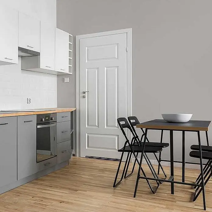 Tadessi Wandfarbe Nebelgrau - Grau, Matt, 1 l - Moderne Küche mit grauen Unterschränken, weißen Oberschränken, heller Holzarbeitsplatte und schwarzem Esstisch mit Klappstühlen.