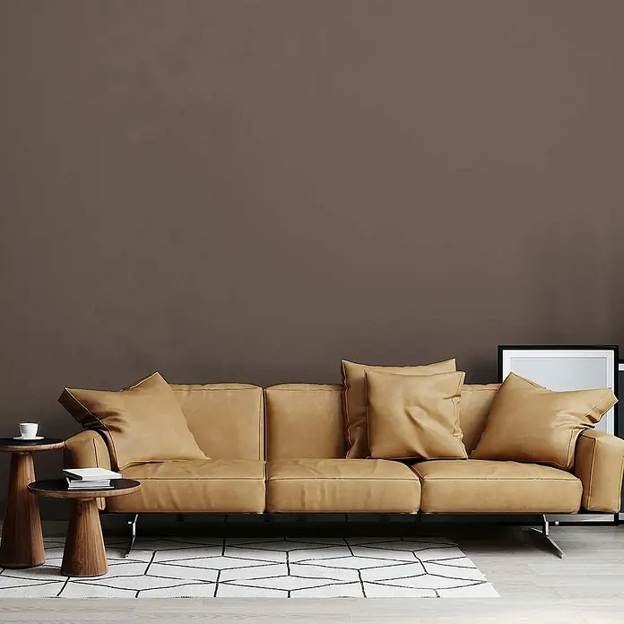 Tadessi Wandfarbe Sand - Braun, Matt, 5 l - Ein beiges Ledersofa mit Kissen in einem modernen Wohnzimmer, ergänzt durch Holztische und einen Teppich.