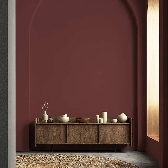 Tadessi Wandfarbe Kastanie - Rot, Matt, 2,5 l - Holz-Sideboard mit drei Fächern und Deko-Objekten in einem Bogenzimmer mit tiefroter Wand.