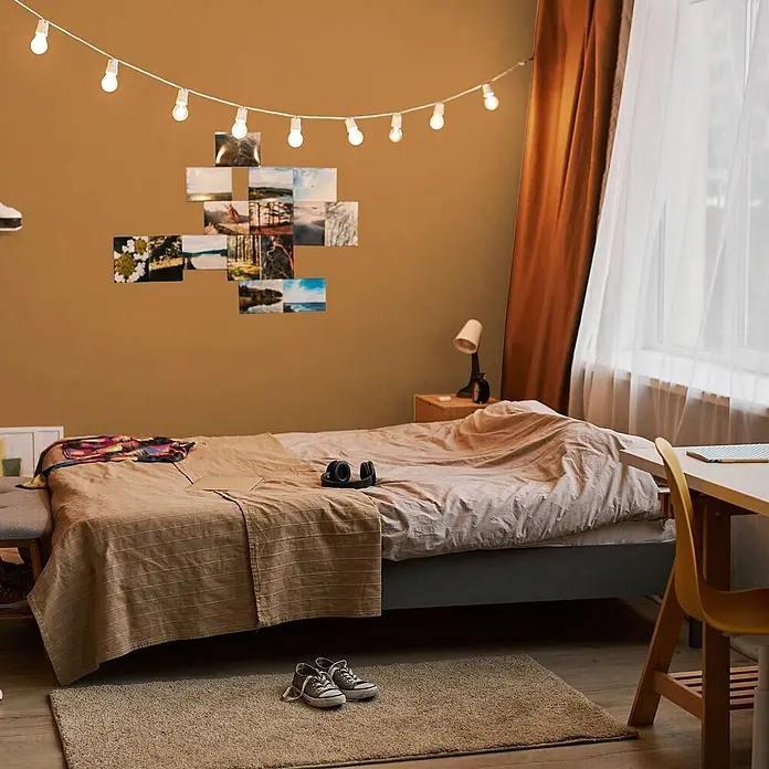 Tadessi Wandfarbe Maronenbraun - Orange, Matt, 5 l - Lichterkette mit runden Glühbirnen beleuchtet eine warm getönte Schlafzimmerwand mit Fotos.