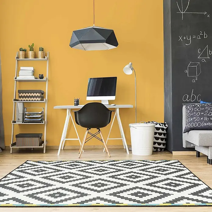 Tadessi Wandfarbe Maisgelb - Gelb, Matt, 1 l - Ein schwarz-weiß gemusterter Teppich mit geometrischem Design auf Holzboden in einem modernen Home-Office.