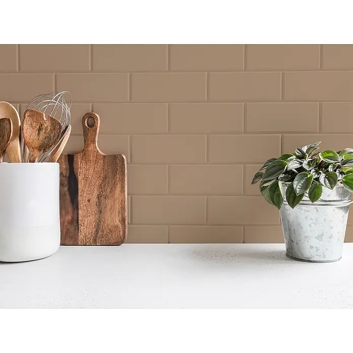 Tadessi Wandfarbe Cognac Mocha - Braun, Matt, 5 l - Verschiedenes Küchenzubehör auf einer Arbeitsplatte: ein weißer Keramik-Utensilienhalter mit Holzbesteck, ein Schneidebrett und eine kleine Topfpflanze.