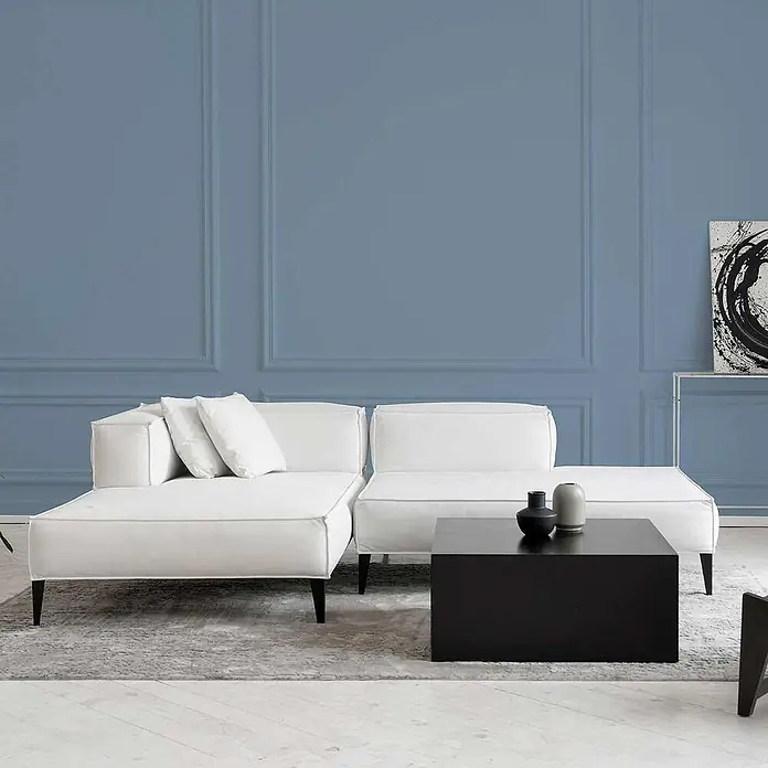 Tadessi Wandfarbe Eisblau - Blau, Matt, 2,5 l - Weißes Modulsofa mit schwarzem Couchtisch in einem modernen Wohnzimmer mit blauen Paneelwänden.