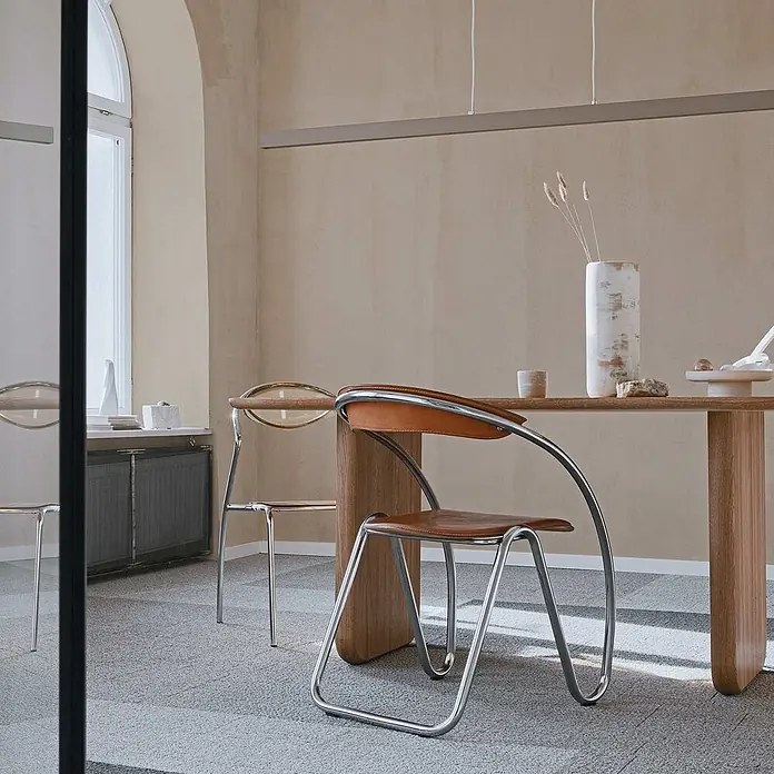 Tadessi Wandfarbe Alpakabeige - Creme, Matt, 5 l - Eleganter Esszimmerstuhl mit brauner Ledersitzfläche und -lehne, charakteristischem geschwungenen Chromgestell an einem Holztisch.