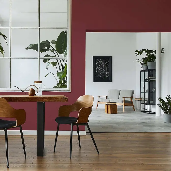 Tadessi Wandfarbe Mahagoni - Rot, Matt, 5 l - Holztisch mit schwarzen Beinen und zwei Holzstühlen mit schwarzen Sitzen in einem modernen Wohnraum.