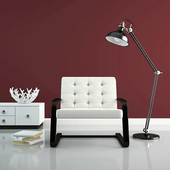 Tadessi Wandfarbe Mahagoni - Rot, Matt, 5 l - Weißer getufteter Sessel mit dunklen Holzdetails und einer hohen schwarzen Stehlampe in einem modernen Wohnraum.