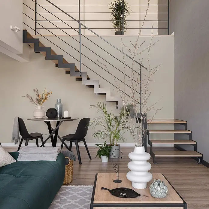 Tadessi Wandfarbe Beigegrün - Beige, Matt, 5 l - Modernes Wohnzimmer mit grünem Sofa, Couchtisch aus Holz, Essbereich mit schwarzen Stühlen und moderner Treppe zum Obergeschoss.