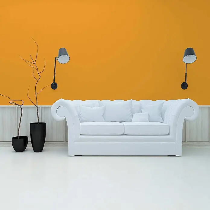 Tadessi Wandfarbe Vanille - Gelb, Matt, 5 l - Weißes getuftetes Sofa mit Kissen in einem modernen Wohnzimmer mit orangefarbener Wand, schwarzen Wandlampen und dekorativen Blumentöpfen.