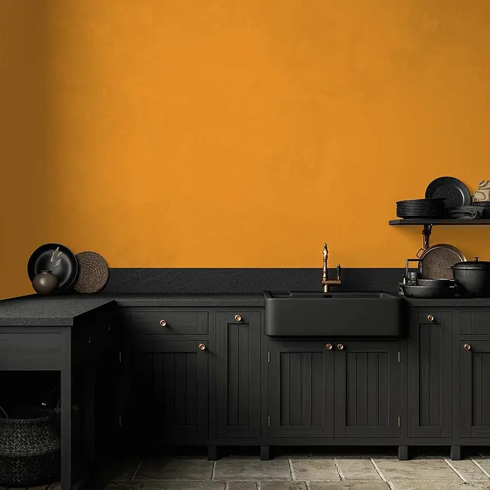 Tadessi Wandfarbe Vanille - Gelb, Matt, 5 l - Moderne Küche mit schwarzen Holzschränken, einer schwarzen Spüle mit Goldhahn und schwarzer Arbeitsplatte vor einer leuchtend orangen Wand.