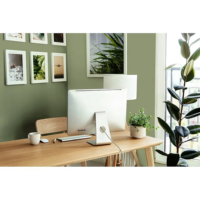 Tadessi Wandfarbe Helles Sage Green - Grün, Matt, 5 l - Ein heller Holzschreibtisch mit einem All-in-One-Computer, Tastatur, Maus und einer Tasse in einem hellen Home-Office mit Pflanzen.