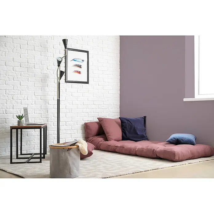 Tadessi Wandfarbe Mauve - Lila, Matt, 2,5 l - Eine rosa Bodenmatratze mit mehreren Kissen bietet bequemes Entspannen in einem modernen Raum.