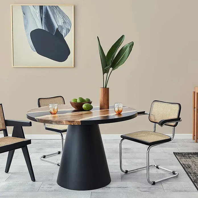 Tadessi Wandfarbe Karamell - Beige, Matt, 1 l - Moderner runder Esstisch mit schwarzem Kegelsockel und gestreifter Holzplatte, ergänzt durch schwarze Korbstühle.