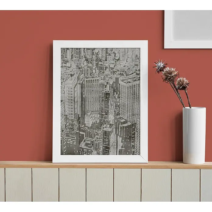 Tadessi Wandfarbe Siena Cherry Rot - Rot, Matt, 2,5 l - Ein weiß gerahmter Kunstdruck einer grauen Stadtlandschaft, auf einem hellen Holzregal vor einer roten Wand.