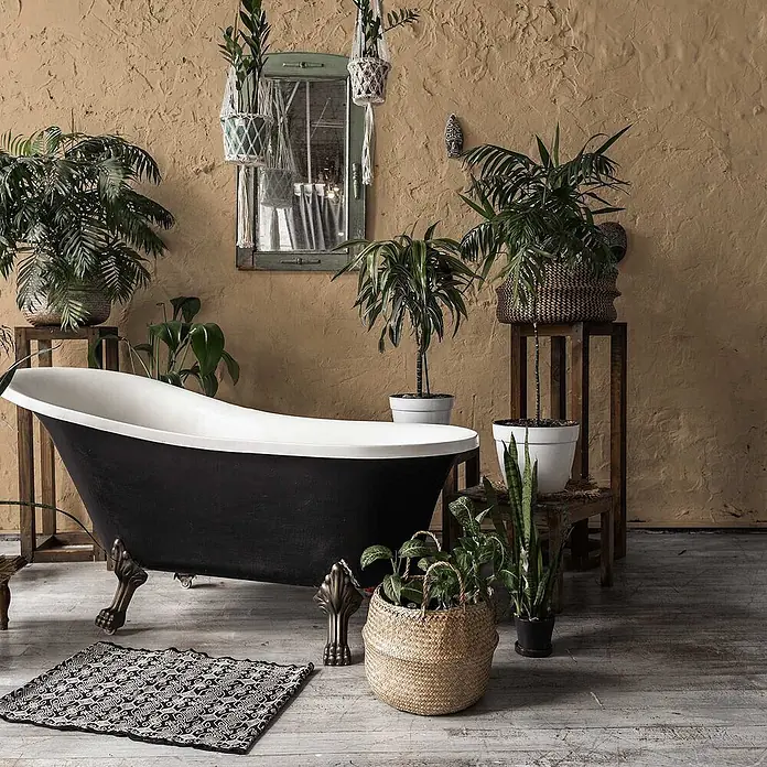 Tadessi Wandfarbe Vanillebeige - Beige, Matt, 5 l - Schwarz-weiße Klauenfußbadewanne mit verzierten Bronzefüßen, in einem üppigen, pflanzenreichen Badezimmer stehend.