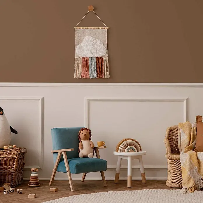 Tadessi Wandfarbe Kaffeebraun - Braun, Matt, 2,5 l - Ein warmes Kinderzimmer mit einer Wolken-Regenbogen-Wanddekoration, einem kleinen blauen Sessel und Holzspielzeug, das einen spielerischen Raum schafft.