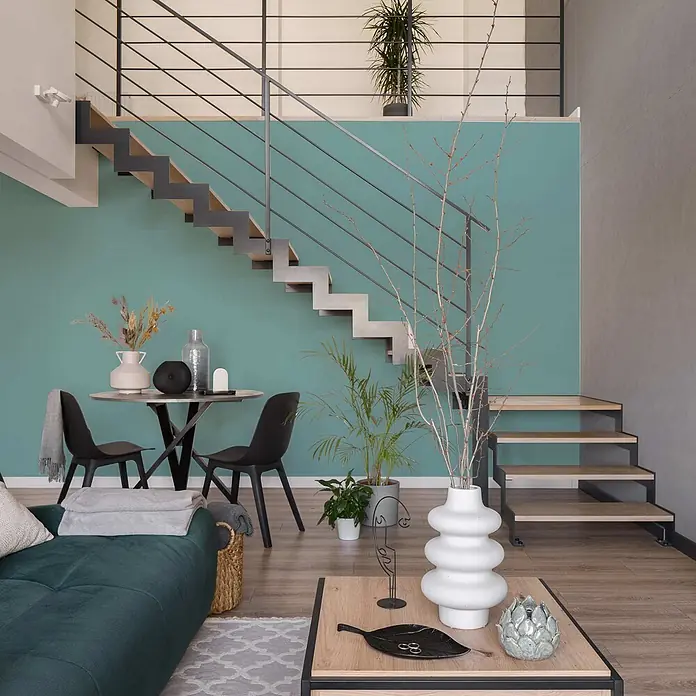 Tadessi Wandfarbe Grünblau - Blau, Matt, 5 l - Modernes Wohnzimmer auf mehreren Ebenen mit türkisfarbener Akzentwand, minimalistischer Treppe und modernen Möbeln.