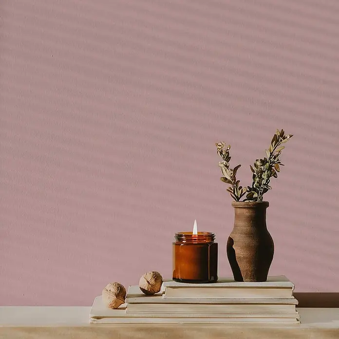 Tadessi Wandfarbe Sandrosa - Pink, Matt, 5 l - Brennende Kerze im Bernsteingefäß, Terrakottavase mit Ästen und Walnüsse auf gestapelten Büchern.
