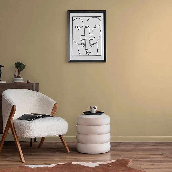Tadessi Wandfarbe Latte - Beige, Matt, 1 l - Weißer Bouclé-Sessel mit Holzbeinen, ein offenes Buch haltend, in einem gemütlichen Wohnzimmer.