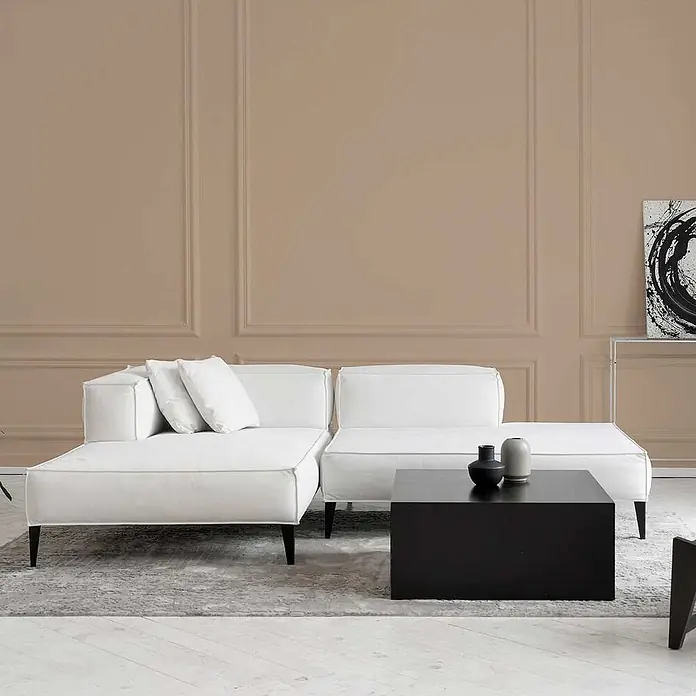 Tadessi Wandfarbe Muskat - Beige, Matt, 5 l - Weißes modulares Ecksofa mit schwarzen Beinen in einem modernen Wohnzimmer, mit einem schwarzen Couchtisch auf einem grauen Teppich.