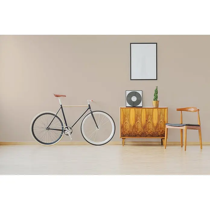 Tadessi Wandfarbe Mandelcreme - Beige, Matt, 2,5 l - Ein schwarzes Fahrrad mit weißen Rädern und braunem Ledersattel lehnt an einer hellbraunen Wand in einem minimalistischen Raum.