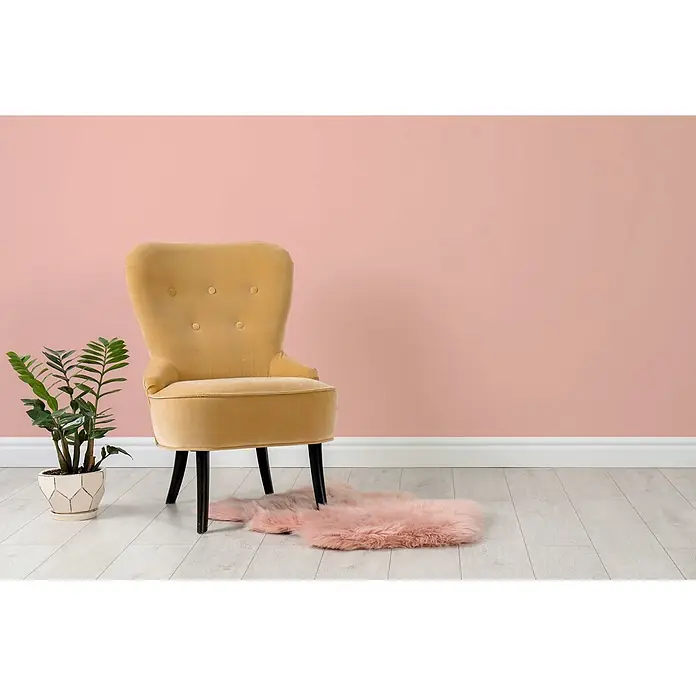 Tadessi Wandfarbe Flamingo Hell - Rosa, Matt, 5 l - Senfgelber Samt-Sessel mit Knopfheftung und dunklen Beinen, in einem Zimmer neben einer Pflanze und einem pinken Teppich.
