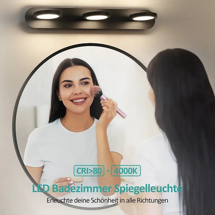 Emke LED-Spiegelleuchte L24 - 15 W, Schwarz - Schwarze LED-Badezimmerspiegelleuchte mit drei runden Lichtern über einem Spiegel, in dem eine Frau Make-up aufträgt.