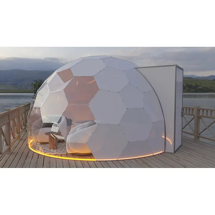 BubbleOrb Gartenkuppel - Durchmesser: 700 cm, Halbtransparent - Geodätisches Kuppelzelt mit Sechseckpaneelen, transparenten und weißen Abschnitten, orange beleuchtet, auf Holzdeck am See.