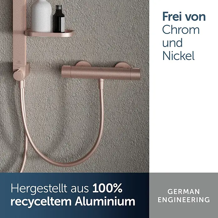 Ideal Standard Alu+ Thermostatarmatur Ceratherm - Breite: 292 mm, Rosé - Roségoldenes Duschsystem mit Thermostatmischer, Brausestange und Schlauch aus 100% recyceltem Aluminium, an grauer Wand.