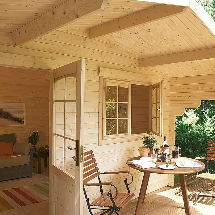 Kiehnholz Gartenhaus Östersund - Außenmaß inkl. Dachüberstand (B x T): 437 x 423 cm, Holz, Natur - Einladendes Holzhaus mit Fenster und Tür offen, Tisch mit Wein und Stühlen auf der Veranda, ein gemütlicher Rückzugsort.
