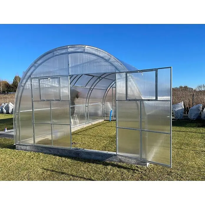 Garten Dream Gewächshaus Oasis, 10mm Polycarbonat - Außenmaß inkl. Dachüberstand (B x T): 400 x 600 cm, Material Seitenwand: Kunststoff, 10 mm, Silber - Großes gewölbtes Polycarbonat-Gewächshaus mit Metallrahmen und offener Tür, draußen auf Betonfundament.