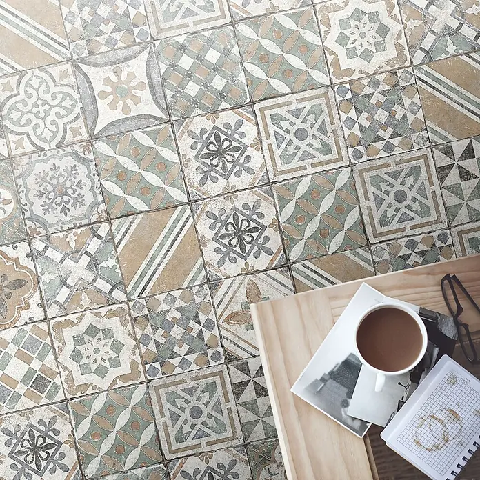 Feinsteinzeugfliese Marrakesh - 20 x 20 cm, Beige Mix, Matt - Antike Bodenfliesen mit vielfältigen geometrischen und floralen Mustern in Beige, Grün und Grau, von oben mit Kaffeetasse daneben.