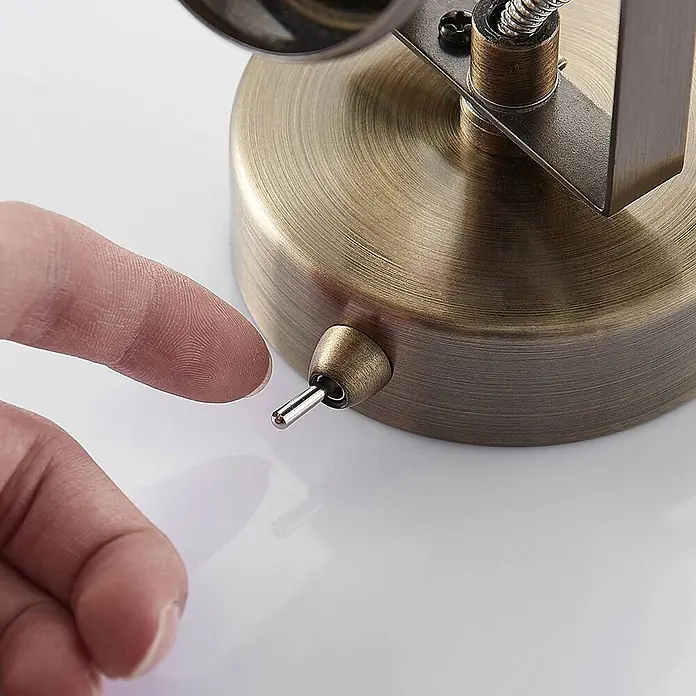 Lindby Wandstrahler Anze - messing / gold, messing / gold, GU10 - Nahaufnahme eines Fingers, der einen antiken Messing-Kippschalter an einem passenden Lampensockel betätigen will.