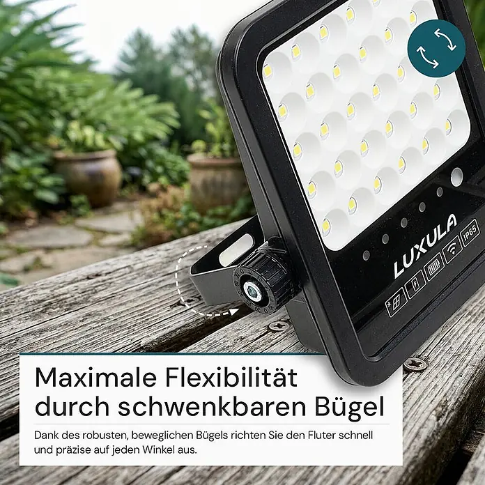 Luxula Solar-Außenwandleuchte LED Solarstrahler - 15 W, L x B x H: 24,9 x 23,2 x 4,8 cm, Schwarz, IP65, 1.650 lm - Schwarzer LED-Fluter auf Holz, mit schwenkbarem Bügel zur flexiblen Winkeleinstellung, in einem Außenbereich.