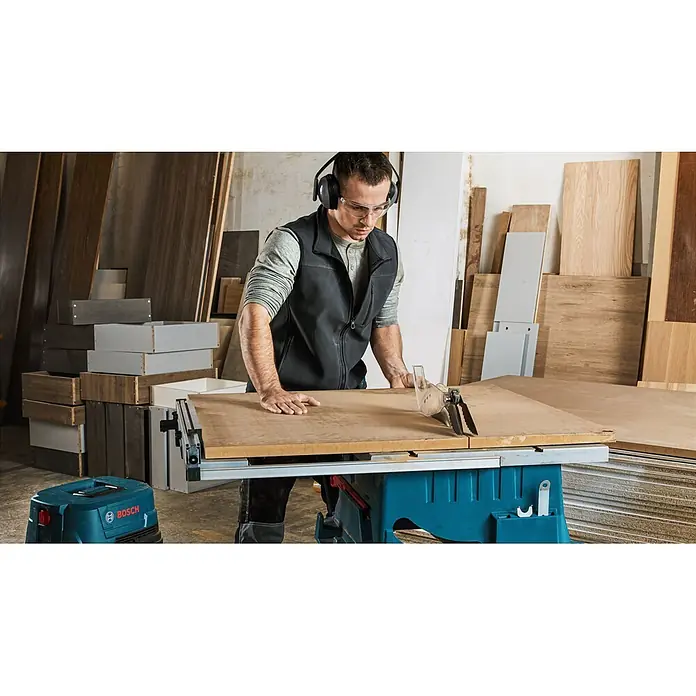 Bosch Professional Tischkreissäge GTS 254 - 1.800 W, Durchmesser Sägeblatt: 250 mm, 4.300 U/min - Mann in Schutzausrüstung schneidet Holz an einer blauen Tischkreissäge.