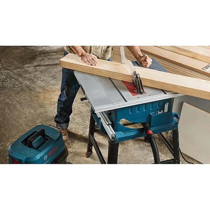 Bosch Professional Tischkreissäge GTS 254 - 1.800 W, Durchmesser Sägeblatt: 250 mm, 4.300 U/min - Eine Person sägt ein Holzbrett mit einer blau-grauen Bosch Tischsäge. Ein blauer Bosch Sauger steht zur Staubabsaugung bereit.