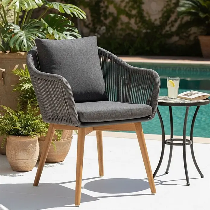 Bene Living Gartenstuhl-Set Solana - 2 Stk., Aluminium mit Teakbeinen, grau, B x T x H: 63 x 59 x 78 cm - Grauer geflochtener Outdoor-Stuhl mit Holzbeinen und Kissen, an einem Pool mit Pflanzen.