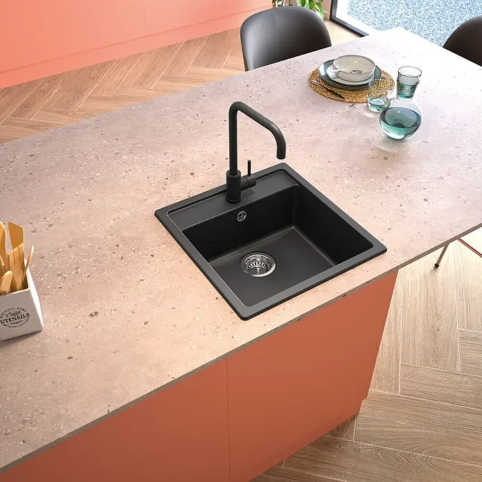 Carea Einbauspüle Essentia - L x B: 49 x 49 cm, Verbundwerkstoff, 80 % Mineralfüllstoff, 20 % hochwertiges Harz - Schwarze Küchenspüle mit Armatur, in eine gesprenkelte Arbeitsplatte einer korallenroten Kücheninsel eingelassen.