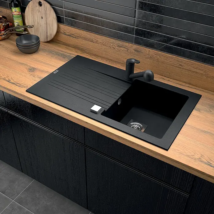 Carea Einbauspüle Muscade - 86 x 50 cm, Schwarz, Hahnloch: Ohne - Schwarze Spüle aus Granitkomposit mit Abtropffläche und schwarzem Wasserhahn, in einer Holztheke montiert.
