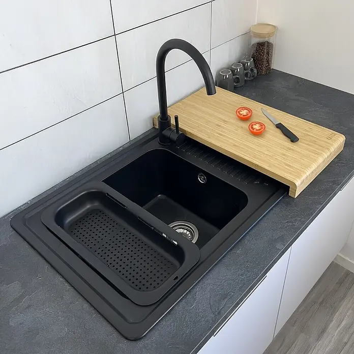 Carea Einbauspüle Venus - 86 x 50 cm, Schwarz, Mit Schneidebrett & Besteckschale - Schwarzes Spülbecken mit integriertem Bambus-Schneidebrett, Messer, Tomaten und Abtropfkorb in einer Küchenumgebung.