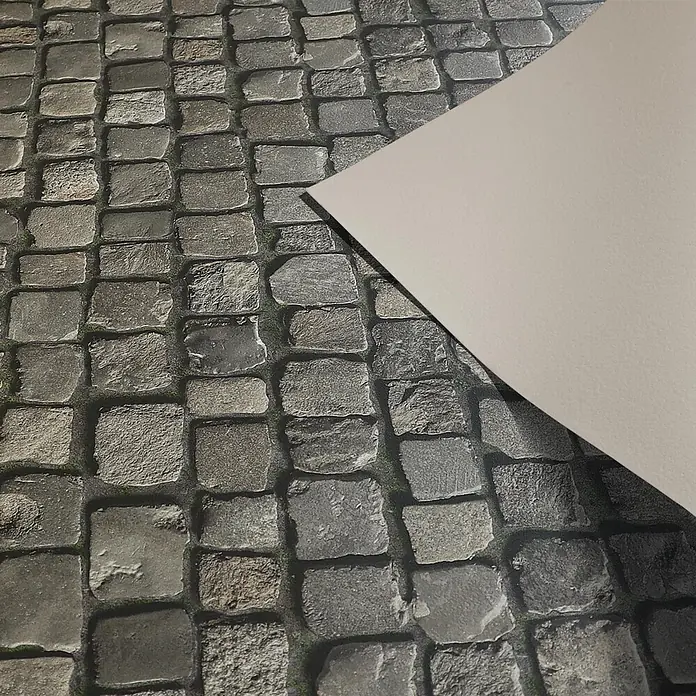 Vinylboden CV-Belag - 50 x 100 cm, Cobble - Helles beiges Papierblatt liegt teilweise auf einem Kopfsteinpflaster.