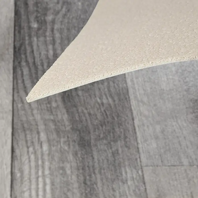 Vinylboden CV-Belag - 1.400 x 200 cm, Holm Oak 999M - Helles beiges, poröses Unterlagsmaterial, seine Schaumtextur zeigend, wird von einem Holzboden abgehoben.