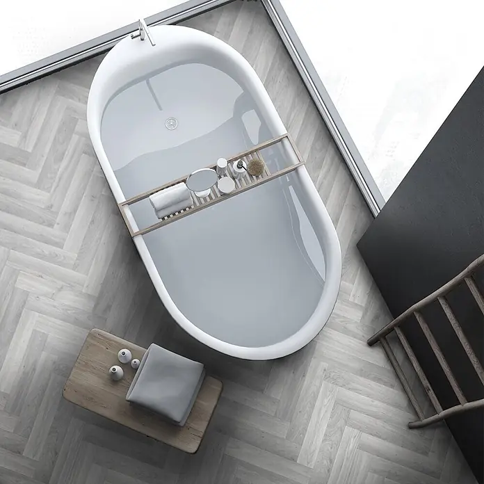 Vinylboden CV-Belag - 400 x 200 cm, Oak Chevron 907M - Moderne weiße Badewanne mit Wasser und einem Holz-Badewannenablage mit Pflegeprodukten auf hellem Fischgrätparkett in einem hellen Badezimmer.