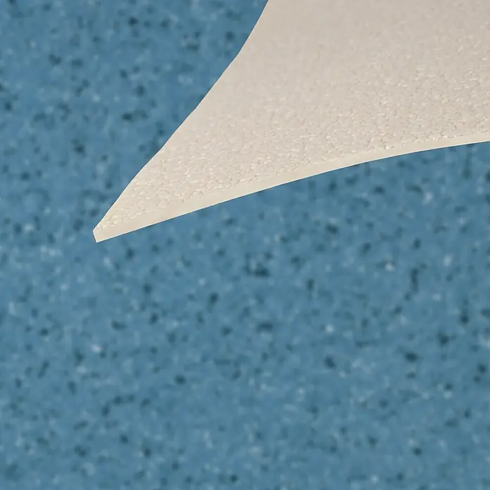 Vinylboden CV-Belag - 1.800 x 200 cm, Mira 707M - Weißes, strukturiertes, dreieckiges Materialstück mit sauberer Kante vor blauem, unscharfem Hintergrund.