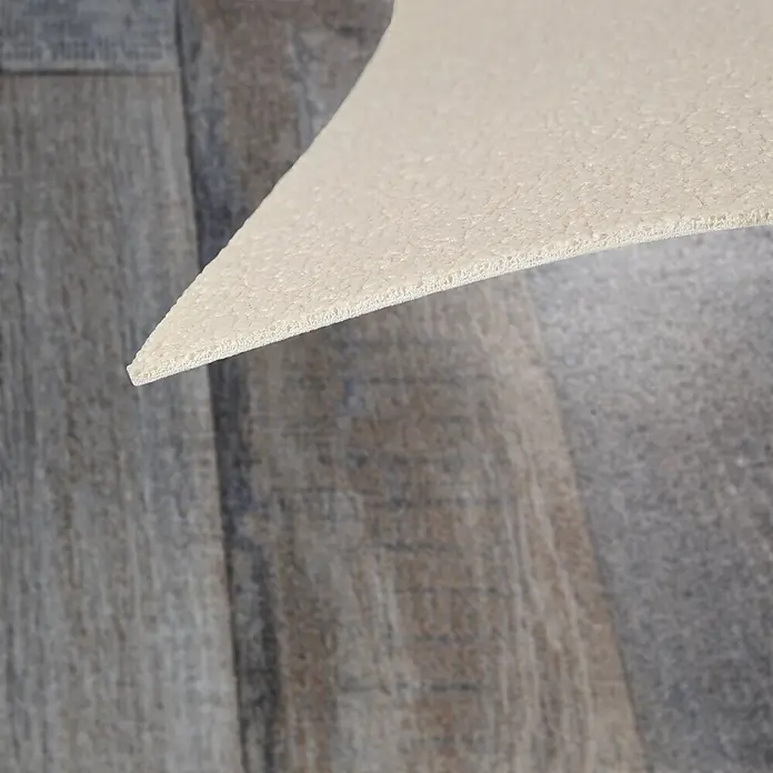 Vinylboden CV-Belag - 1.100 x 100 cm, Cuban Oak 967M - Hellbeiges Schaumstoffunterlage mit texturierter Oberfläche, teilweise von einem Holzfußboden abgehoben.
