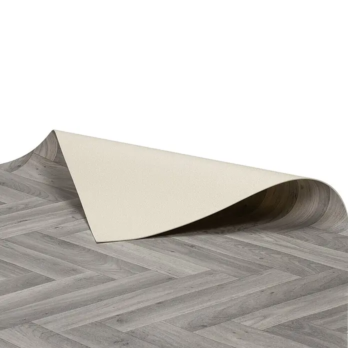 Vinylboden CV-Belag - 400 x 200 cm, Oak Chevron 907M - Grauer Bodenbelag in Holzoptik im Fischgrätmuster, eine Ecke hochgeklappt zeigt die helle, unstrukturierte Unterseite.