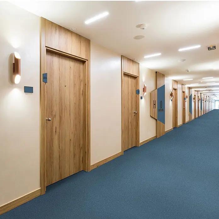Vinylboden CV-Belag - 1.800 x 200 cm, Mira 707M - Langer Hotelkorridor mit Holztüren und blauem Teppich.