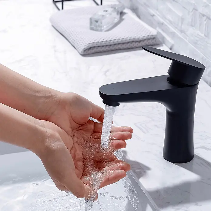 LOMAZOO Waschtischarmatur MARY - Schwarz - Moderner schwarzer matter Einhandmischer, der Wasser über Hände in einem weißen Waschbecken gießt.